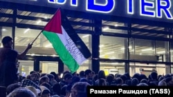 Човек вее палестинско знаме со порака на која пишува „Дагестан стои покрај тебе“ за време на пропалестинскиот митинг на аеродромот во Махачкала