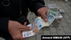 Уличен продавач покажува банкноти со српскиот динар во градот Грачаница, централно Косово, 1 март 2024 г.