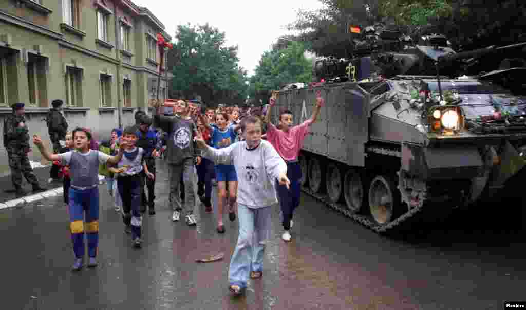 Djeca trče pored britanskog tenka nakon što je stigao u Podujevo 18. juna 1999. godine. Trg je danas proširen svježe zasađenim drvećem.
