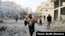 Un bărbat palestinian cară o fetiță rănită la locul loviturilor israeliene, în Khan Younis, în sudul Fâșiei Gaza, la 14 octombrie 2023.