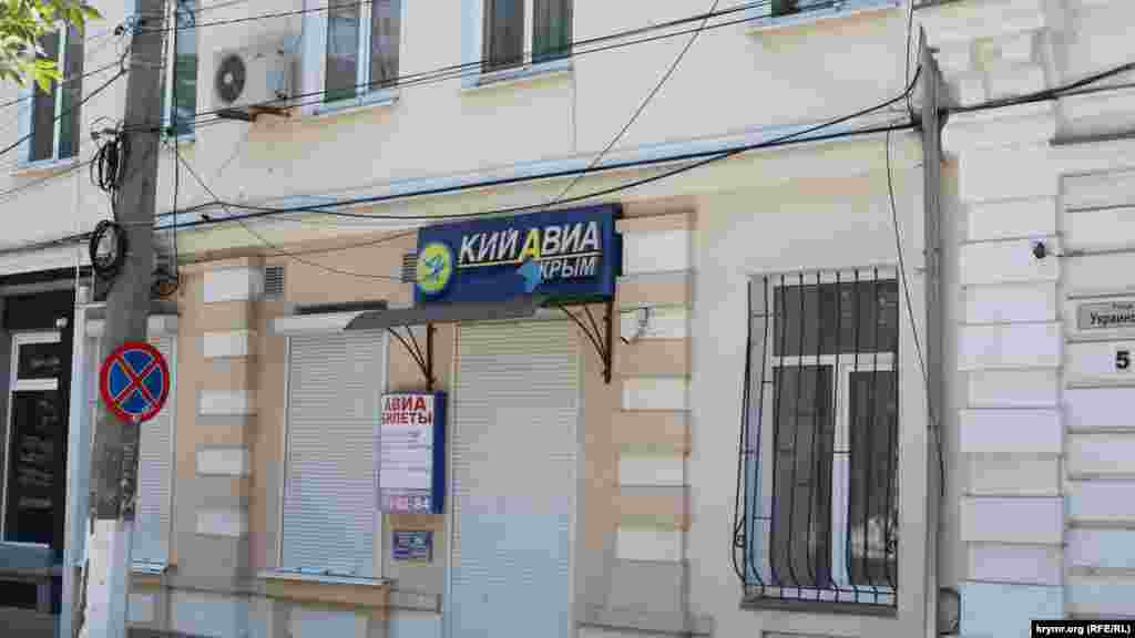 Kefeniñ merkezinde Ukrainskaya soqağında Kyiv-Aqmescit seferlerini kerçekleştirgen «Kiy-Avia» ava şirketiniñ levhası alâ daa bar