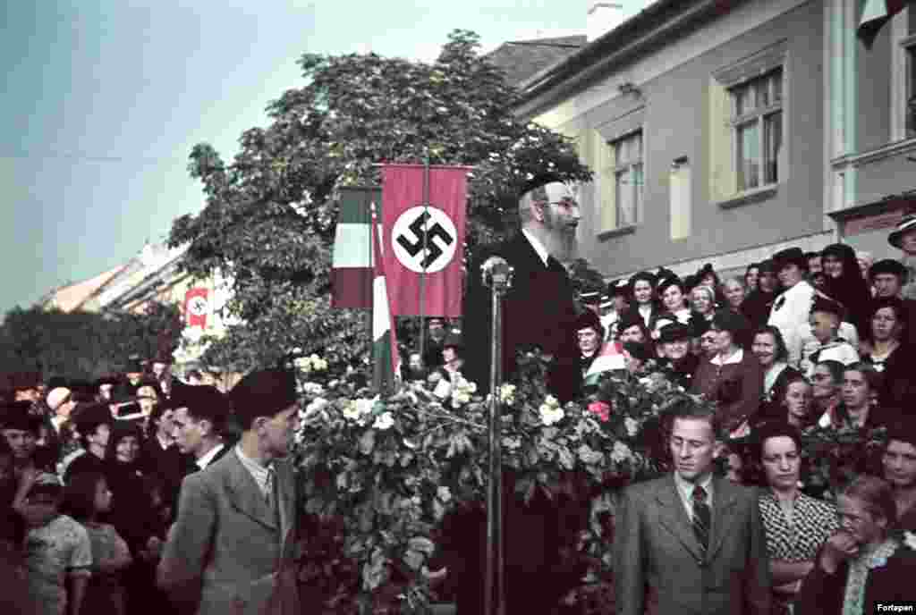 Un rabin vorbind mulțimii pe fundalul unei svastici naziste, în timp ce trupele maghiare fasciste intră în orașul Bistrița.