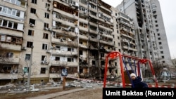 Киев, 25 феврали соли 2022. Писарбачае дар муқобили бинои бар асари ҳамлаҳои Русия осебдидаи ҳавлии хонааш нишастааст