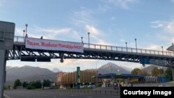 Алматының Әл-Фараби мен Асқаров көшелерінің қиылысындағы көпірде ілініп тұрған Жанболат Мамайды босатуға үндеген плакат. Көп ұзамай полиция плакатты алып тастады, оны ілгендерді ұстады. 3 маусым 2022 жыл.
