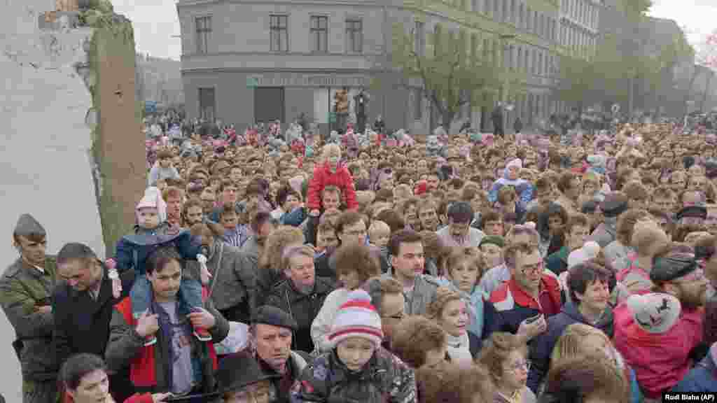 Хората се стичат през процеп в стената на 11 ноември 1989 г. На източногерманските войници е наредено да стоят настрана. На 9 ноември тогавашният секретар по въпросите на информацията на Германската социалистическа партия - Гюнтер Шабовски, заявява, че от полунощ източногерманците ще могат свободно да напускат ГДР. Пада физическото разделение между Източен и Западен Берлин.