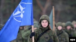 O femeie soldat prezintă drapelul NATO la ceremonia de închidere a exercițiului militar multinațional Iron Sword 16 în apropiere de Vilnius, 2 decembrie 2016
