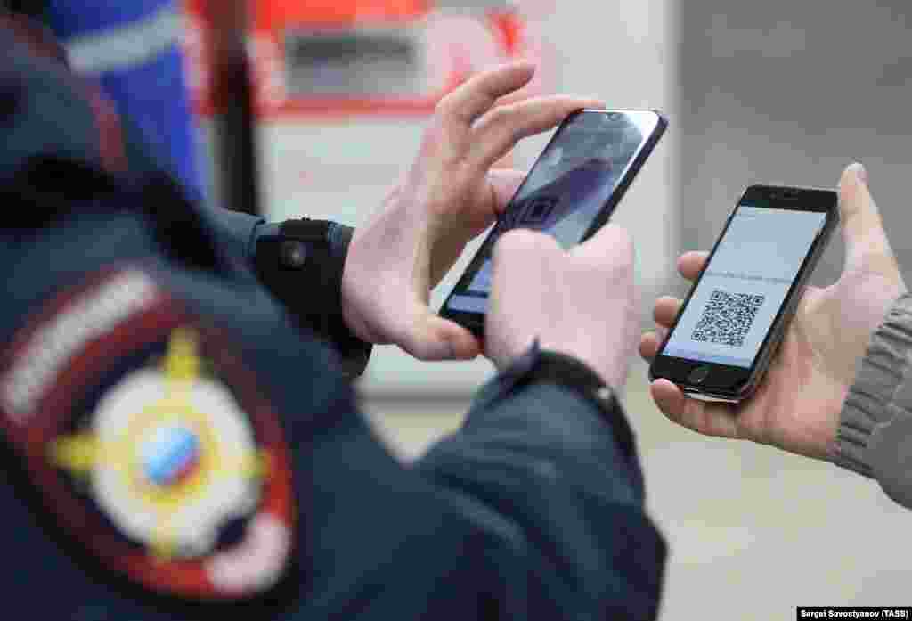 Полициски службеник гледа на QR-кодот на паметен телефон на патник за време на проверка на лична карта на станицата „Планернаја“ во московското метро на 15 април во Москва, Русија. Според системот за дигитални дозволи, воведен од московската влада, кој стана задолжителен од 15 април, луѓето треба да аплицираат за дозволи за патување со јавен превоз или возило низ градот.