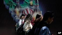 Femei iraniene fără eșarfa obligatorie pe cap trec pe lângă un banner din Teheran, în aprilie.