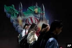 Femeile iraniene fără eșarfă obligatorie sau hijab trec pe lângă un banner în Teheran în aprilie.