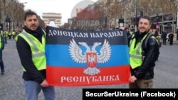 Флаг группировки «ДНР» во время протестов в столице Франции. Его держат: Фабрис Сорлин (слева) и Ксавье Моро