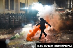 Маскиран полицаец клоца димна бомба покрај зградата на грузискиот парламент во Тбилиси на 29 ноември за време на втората ноќ од протестите што избувнаа откако грузиската влада објави прекин на преговорите за пристап во ЕУ.