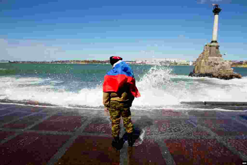 Мужчина с российским флагом на спине стоит на берегу моря в Севастополе в штормовую погоду в марте. Когда Крымский полуостров прочно находился под контролем России, 7 апреля Россия подготовила почву для войны: вооружённые пророссийские группы в Донецке и Луганске ворвались в правительственные учреждения. Киев ответил объявлением о начале «контртеррористической» операции