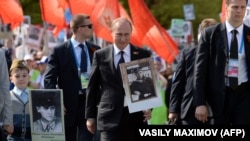 Președintele rus Vladimir Putin (centru) poartă un portret al tatălui său la marșul Regimentului Nemuritor în timpul sărbătoririi Zilei Victoriei, la Moscova, pe 9 mai 2015.