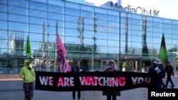 Mulți activiști de mediu marchează începutul COP28 departe de Dubai. În imagine, protestatari cu o pancartă pe care scrie „Vă urmărim” în fața sediului BBC din Salford, Marea Britanie. (Foto: REUTERS/Phil Noble)