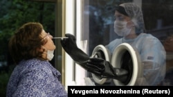 Russia -- A staff member of AltraVita fertility clinic takes a swab from an outdoor booth as a woman undergoes a test for the coronavirus disease (COVID-19) in Moscow, June 11, 2020