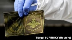 Украинский криминалист показывает нашивки, найденные на теле российского солдата, эксгумированного в селе Заваловка Киевской области. 11 мая 2022 года