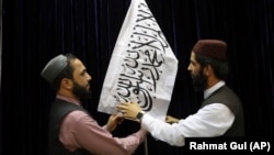 Taliban officials arrange a Taliban flag before the start of the group's press conference on August 17, at which the militants sought to assuage fears that they would reestablish a repressive regime in Afghanistan similar to that of their previous stint in power in 1996-2001.