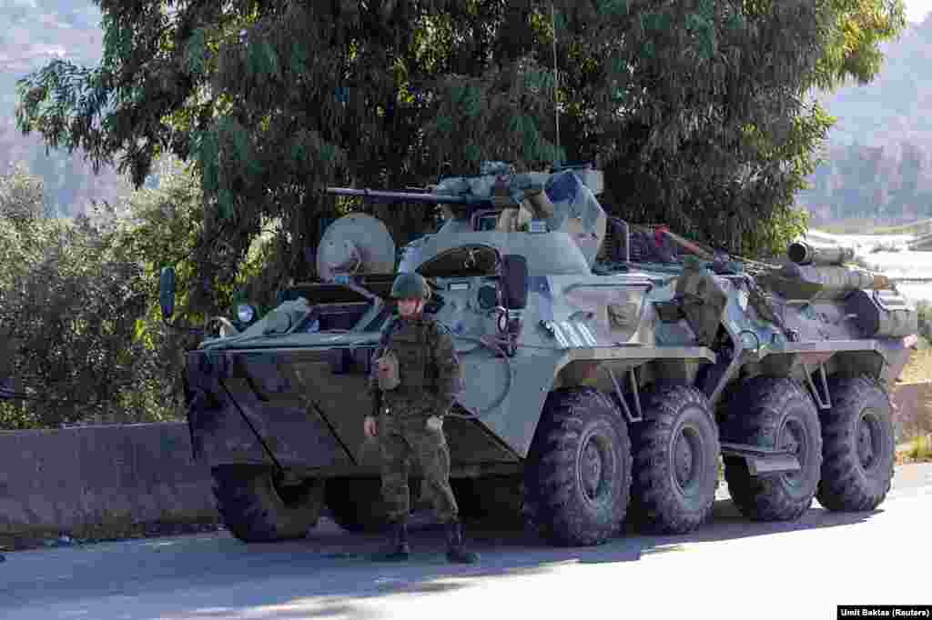 Un soldat rus de gardă lângă un vehicul blindat, în apropierea bazei aeriene Hmeimim. Într-o declarație scrisă despre recenta sa evadare din Siria, președintele alungat de la putere, Bashar Al-Assad, spune că a fost transportat inițial de la Damasc la baza Hmeimim, în timp ce rebelii înaintau rapid spre capitala siriană. În cele din urmă, a fost dus pe calea aerului în Rusia, pe 8 decembrie, după ce baza rusă „a fost atacată intens cu ajutorul dronelor”.