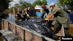 Voluntarii încarcă saci cu cadavre recuperate pe 16 iunie din casele inundate, după ce apele s-au retras în urma ruperii barajului Kahovka