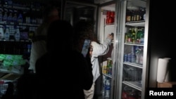 Cumpărătorii luminează rafturile cu telefonul mobil într-o alimentară din Barcelona, Spania, în timpul penei de curent din 28 aprilie 2025