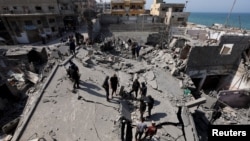 Mai mulți palestinieni inspectează locul unui atac israelian asupra unei clădiri rezidențiale, în Deir Al-Balah, în centrul Fâșiei Gaza, 18 martie 2025. 