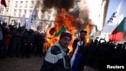 Un susținător al partidului ultranaționalist Renașterea din Bulgaria în fața unei efigii în flăcări a lui Christine Lagarde, președintele Băncii Centrale Europene, și a unui steag al UE, în timpul unei demonstrații împotriva planurilor țării de a adera la zona euro.