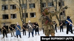 Воен инструктор ги учи цивилите кои држат дрвени копии на пушки калашников, за време на тренинг сесија во напуштена фабрика во украинскиот главен град Киев на 30 јануари 2022 година.