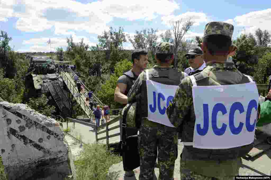 Українські офіцери Об'єднаного центру контролю та координації та співробітники ОБСЄ спостерігають за тим, як люди проходять через зруйнований міст між підконтрольною Україні територією та територією, яку контролюють гібридні російські збройні формування. Станиця Луганська, 1 серпня 2019 року 