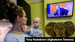 Russiýaly aýal çagasy bilen prezident Wladimir Putiniň çykyşyna tomaşa edýär. 